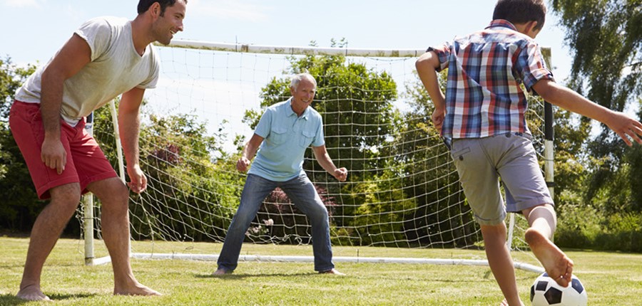Abuelo, padre e hijo jugando al fútbol en el jardín